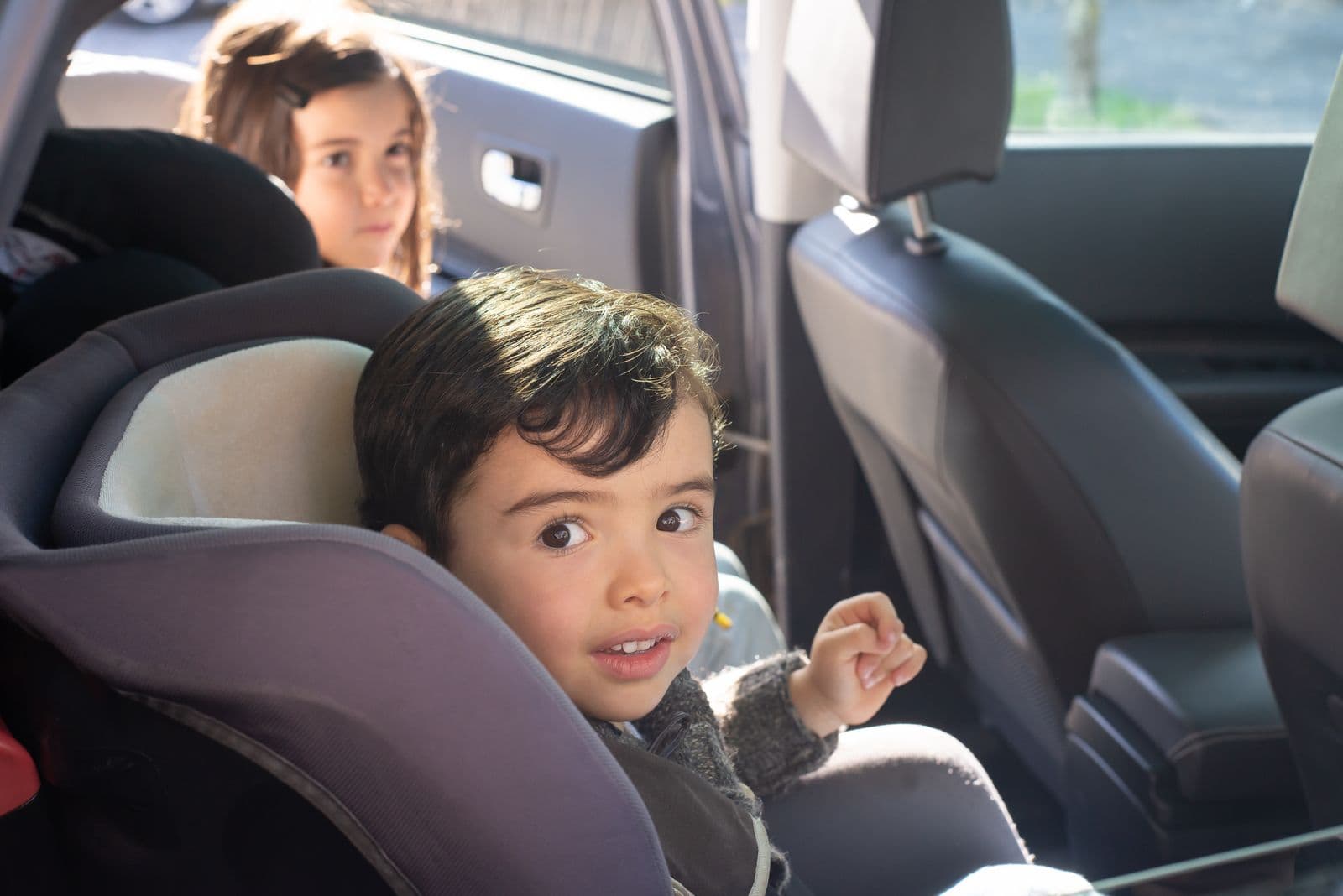 Two young children strapped into child seats on the back seat of a car